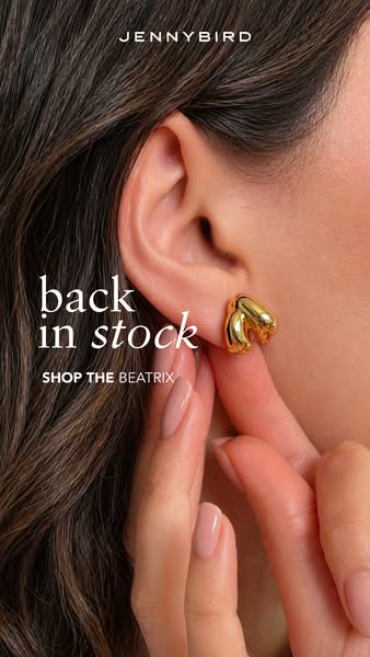 A close up of a woman wearing gold earrings. The text reads 'back in stock SHOP THE BEATRIX'.