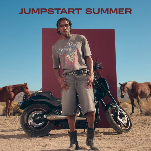 This ad features a man standing in a desert landscape next to a motorcycle. Text overlay states "JUMPSTART SUMMER&q