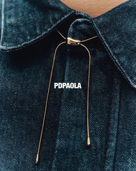 This ad showcases a gold necklace from PDPAOLA. The necklace is worn with a denim shirt.