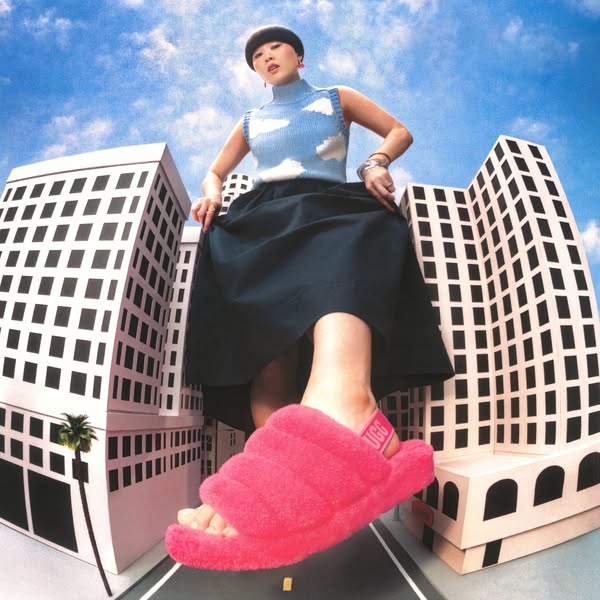An ad for UGG Fluff Yeah slides that shows a model standing in an urban scene as a giant wearing the slides, highlightin