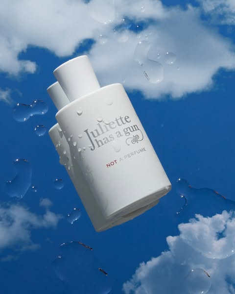 This ad showcases a bottle of Juliette has a gun Not a Perfume fragrance against a bright blue sky with puffy white clou