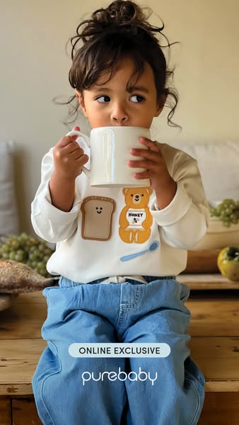 An advertisement from Purebaby featuring a young child wearing a white long-sleeved shirt with a bear and toast graphic 