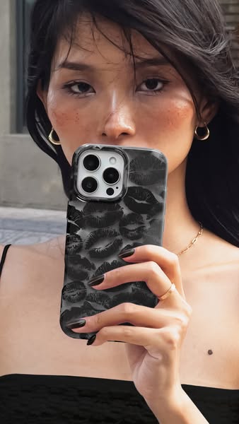 This image ad features a woman holding up a phone with a distinctive case featuring an all-over lip print pattern in bla