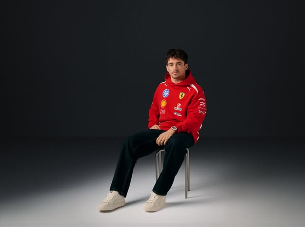 This ad features Charles LeClerc wearing a red Ferrari Racing hoodie and PUMA sneakers, seated on a stool in front of a 