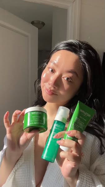 An advertisement showcasing the Weleda Skin Food collection, featuring a person presenting three products and smiling at