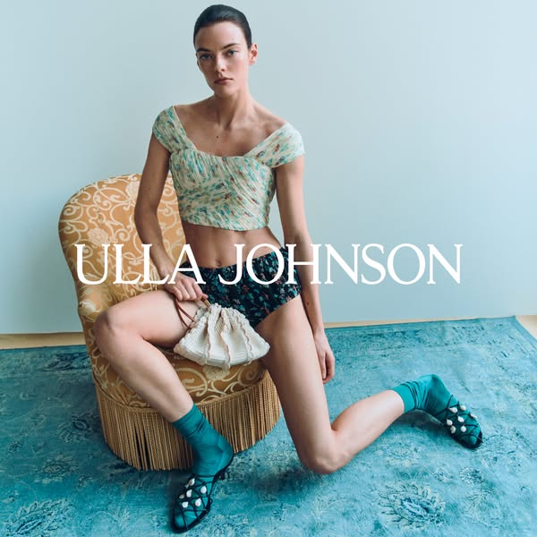 An image ad for Ulla Johnson features a model wearing the brand's clothing. The model is seated and holding a small