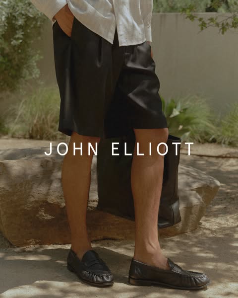 This image ad features a person wearing John Elliott shorts and loafers. The brand name is centered in the ad.