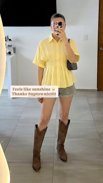 A woman in a yellow shirt, olive shorts, and cowboy boots poses in front of a mirror in what looks to be a story post on