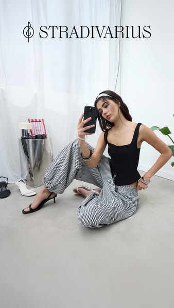 An ad for Stradivarius featuring a woman posing for a selfie wearing a black top and houndstooth pants, promoting the br