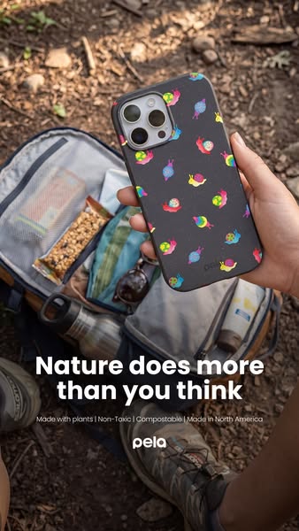 A lifestyle shot of a Pela phone case being held by a person who is also wearing hiking boots and has an open backpack. 