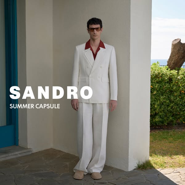 This image ad showcases a men's double-breasted white suit from the Sandro Summer Capsule collection, modeled agains
