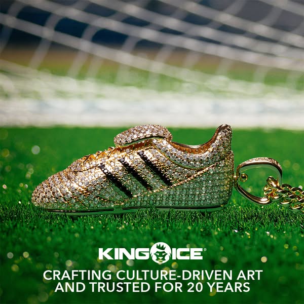 This image ad features a close-up of a jeweled soccer cleat pendant against a background of a soccer field and net. It h