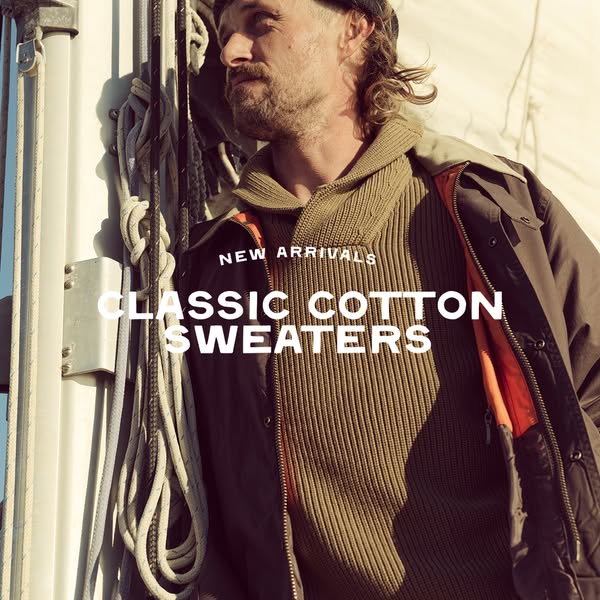 This image ad for classic cotton sweaters features a man in a neutral-toned sweater and jacket, standing in an outdoor e