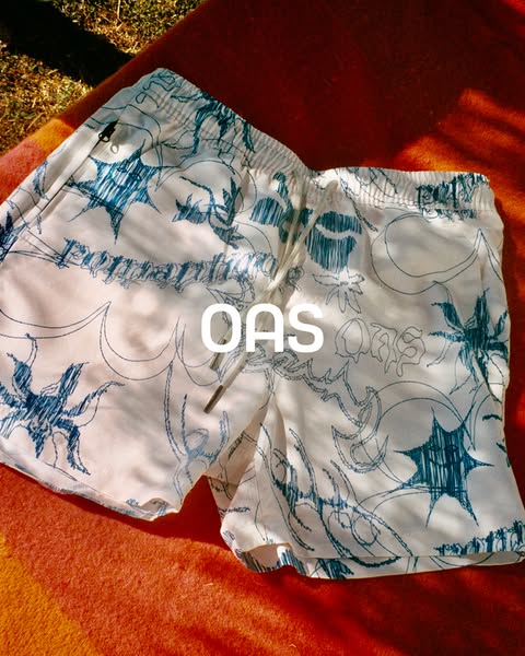 This ad is for OAS swimwear, showcasing a pair of white swim trunks with a blue abstract pattern. The trunks are laid on