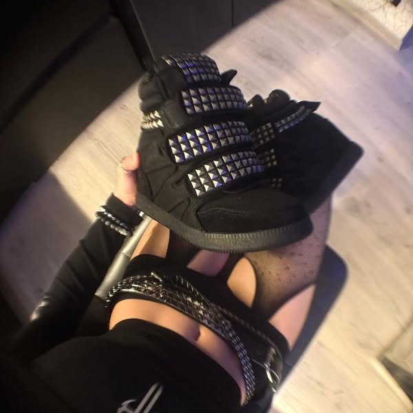 The ad features a woman holding up a black high-top sneaker with pyramid stud embellishments. The focus is on showcasing