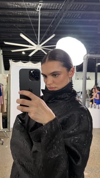 A woman is taking a selfie in a studio, potentially advertising clothing or a makeup look.
