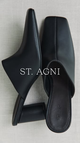 Image ad showcasing a pair of black ST. AGNI mules on a neutral background.