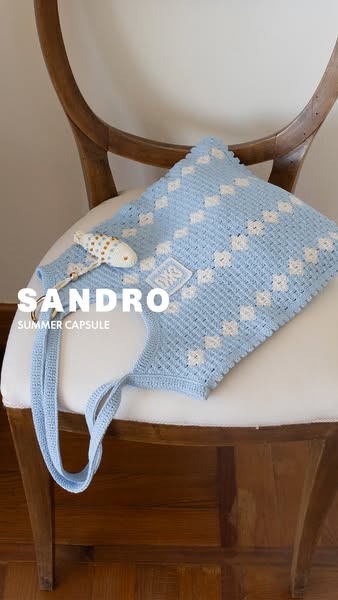 This ad showcases a blue crocheted Sandro tote bag from the brand's summer collection.