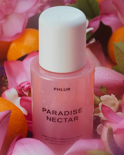 This ad showcases Phlur's Paradise Nectar Hair & Body Fragrance Mist, presenting it amidst a backdrop of pink fl