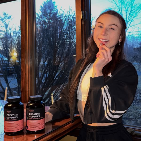An image ad showcasing Legion brand creatine gummies, featuring a woman holding a gummy and standing next to two contain