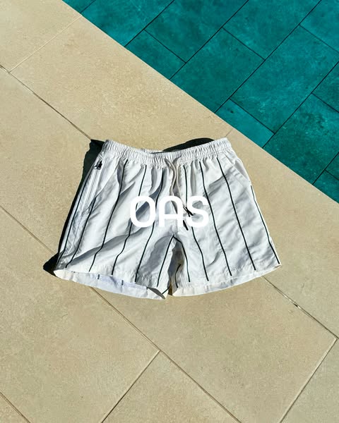 This image ad features white and black striped OAS brand swim shorts. The shorts are set against a backdrop split betwee