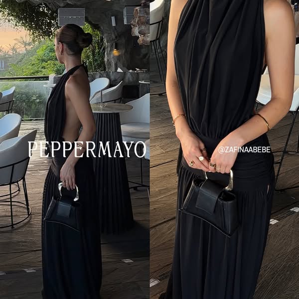 This image ad showcases a black maxi dress and handbag from the brand Peppermayo. A woman models the dress in a restaura