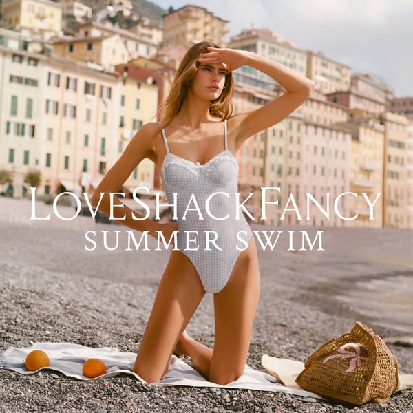 This ad showcases a LoveShackFancy swimsuit with a gingham pattern. The backdrop features a picturesque coastal village 
