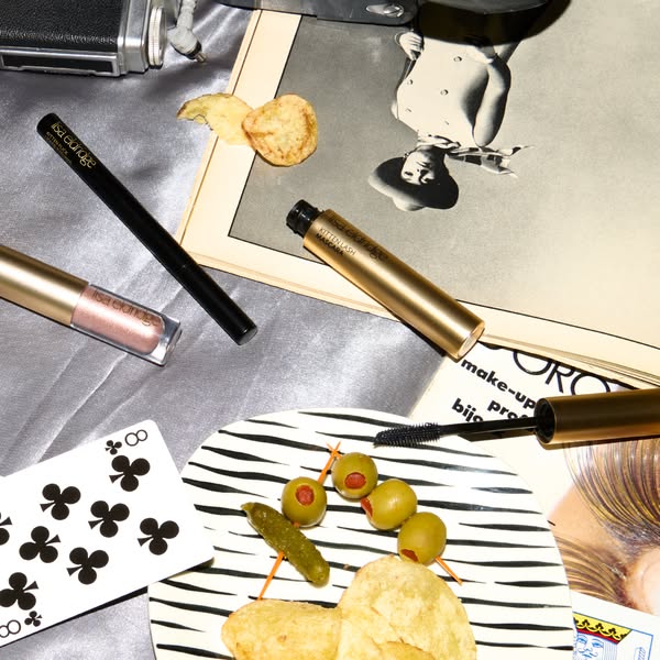 This ad features Isa Eldridge makeup products in a flatlay style, surrounded by props like a vintage camera, playing car