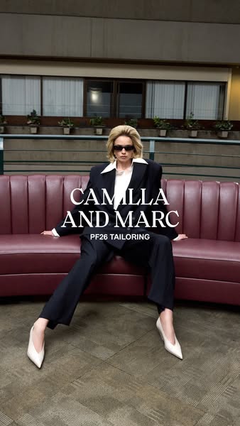 This image ad by Camilla and Marc showcases a blond woman sitting on a red couch in a black tailored suit and cream heel