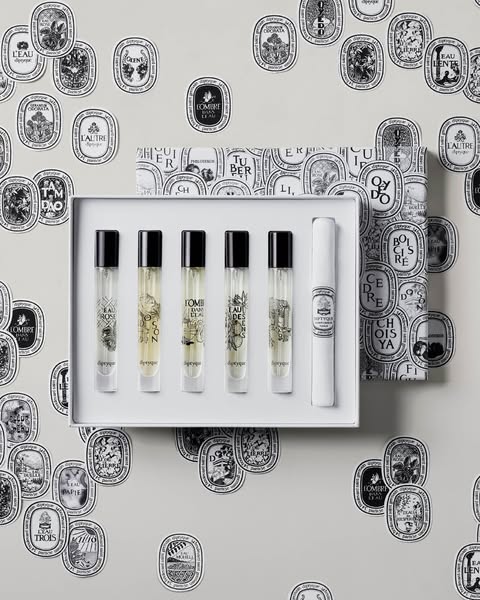 This ad displays a set of Diptyque fragrances in their packaging, presented in a stylized, visually appealing manner. Th