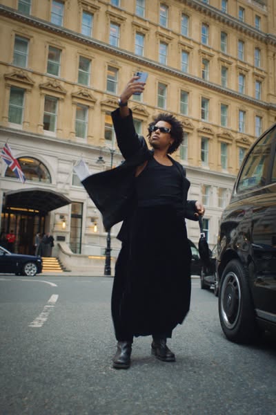 The ad features a person taking a selfie with a smartphone while standing on a street in front of a building and a taxi.