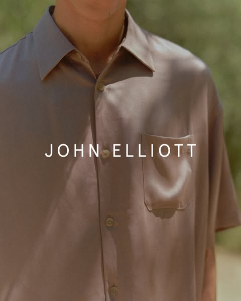 This image shows a John Elliott shirt being worn by a light skinned individual with the brand name superimposed in white