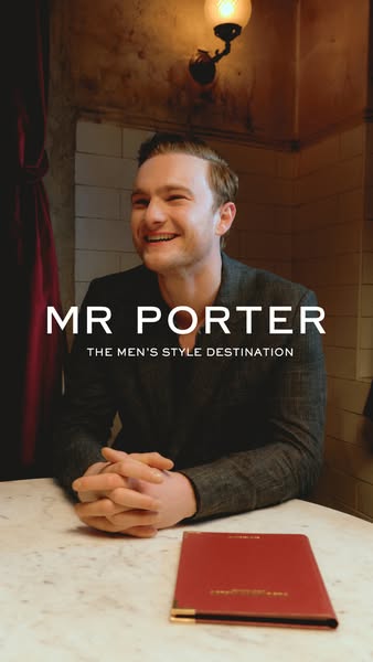 This image ad presents Mr Porter as a curated style destination for men by featuring a smiling man sitting at a table, s