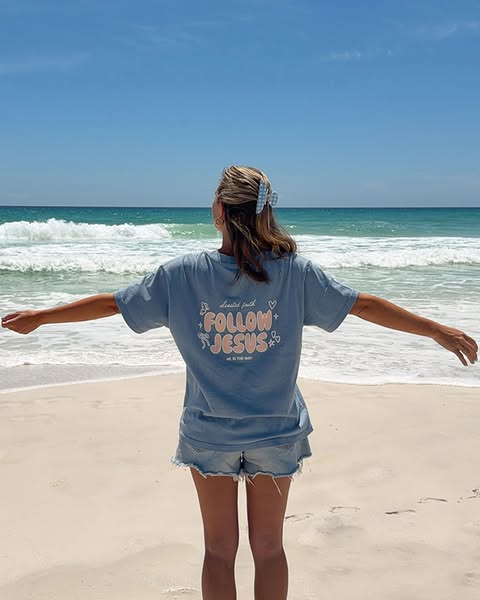 This ad features a woman standing on a beach, facing away from the camera, wearing a blue t-shirt with the text 'dev
