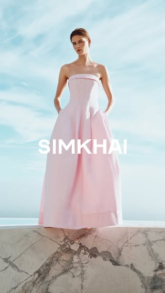 An image ad for SIMKHAI featuring a model in a pink dress, set against a bright, sunny sky.