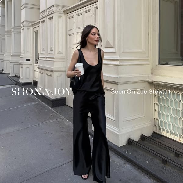 A stylish woman is seen wearing a matching black satin top and pants outfit, with the branding appearing on the left, an
