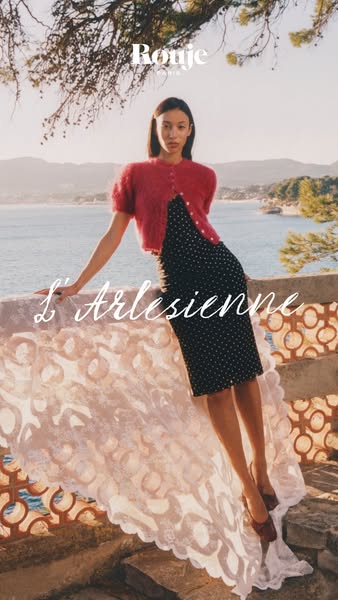 This image ad for Rouje features a model standing in front of a scenic ocean view. She is wearing a polka dot dress and 