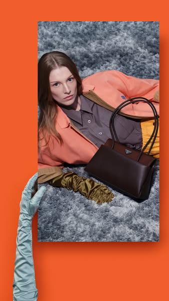 This image ad for Prada features a model laying on a gray faux fur surface next to a Prada handbag and a pair of satin g