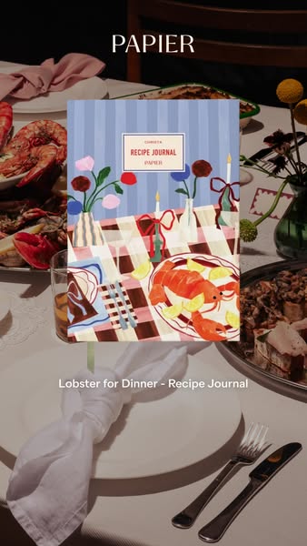 This ad features a Papier recipe journal on a table with food. The journal has an illustration of a lobster dinner on th