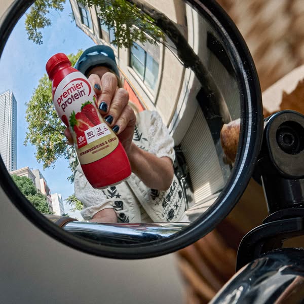 This ad features a Premier Protein Strawberries & Cream shake being held by a person on a scooter, as viewed through