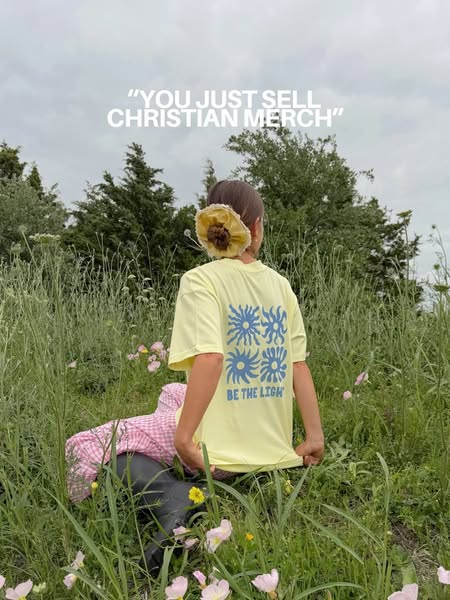 The image is an advertisement for a t-shirt featuring a daisy-like flower design and the phrase "Be the Light"