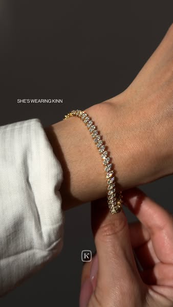 This ad showcases a gold, diamond tennis bracelet from Kinn worn on someone's wrist.