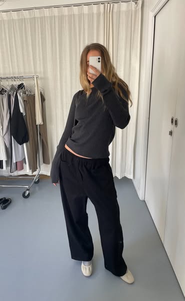 This ad features a woman wearing a black top and black pants in what appears to be a dressing room. She's taking a m