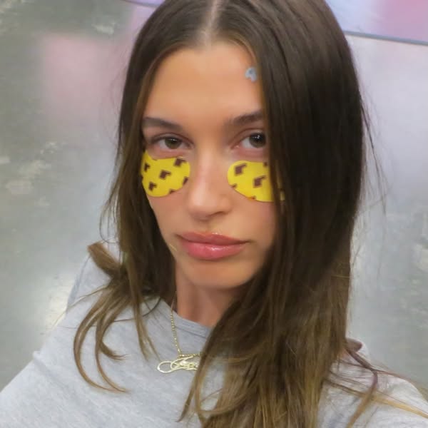 This ad features an image of Hailey Bieber wearing yellow eye masks with brown logos. She is looking directly at the cam