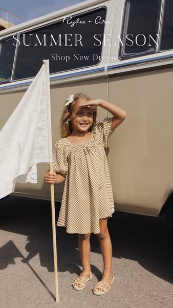 This image ad for Rylee + Cru features a young girl in a printed dress, holding a flag and smiling towards the light in