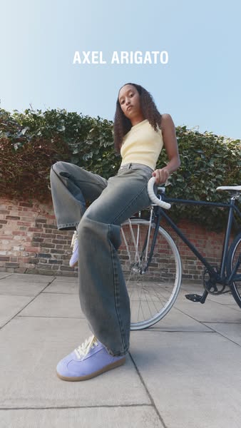 A full-shot image of a person sitting on a bike and wearing Axel Arigato shoes. The focus is on showcasing the shoes.