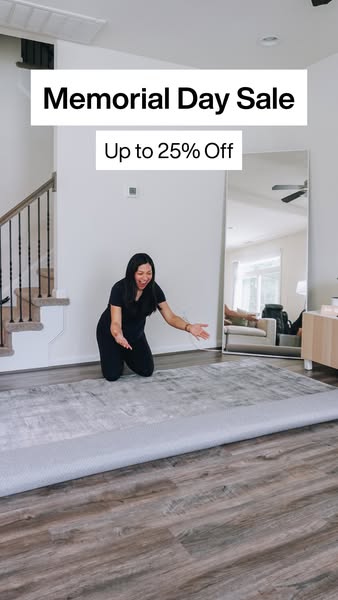 A woman is unrolling a gray area rug. The ad promotes a Memorial Day Sale that is up to 25% Off.