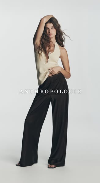 This ad showcases a model wearing a flowy outfit comprised of a light colored top and black, wide-legged bottoms. The br