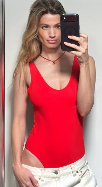 A woman takes a selfie in a red bodysuit. This image demonstrates the style of the bodysuit on a person.