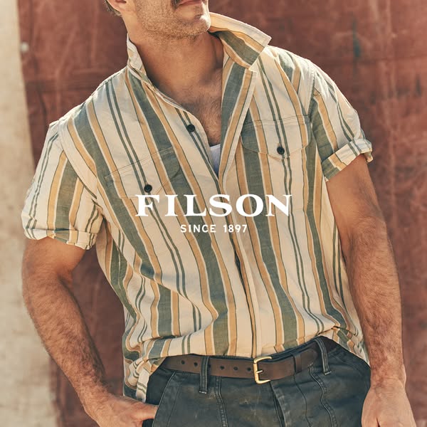 This ad features an image of a person wearing a striped button-down shirt and trousers, with the FILSON brand logo super